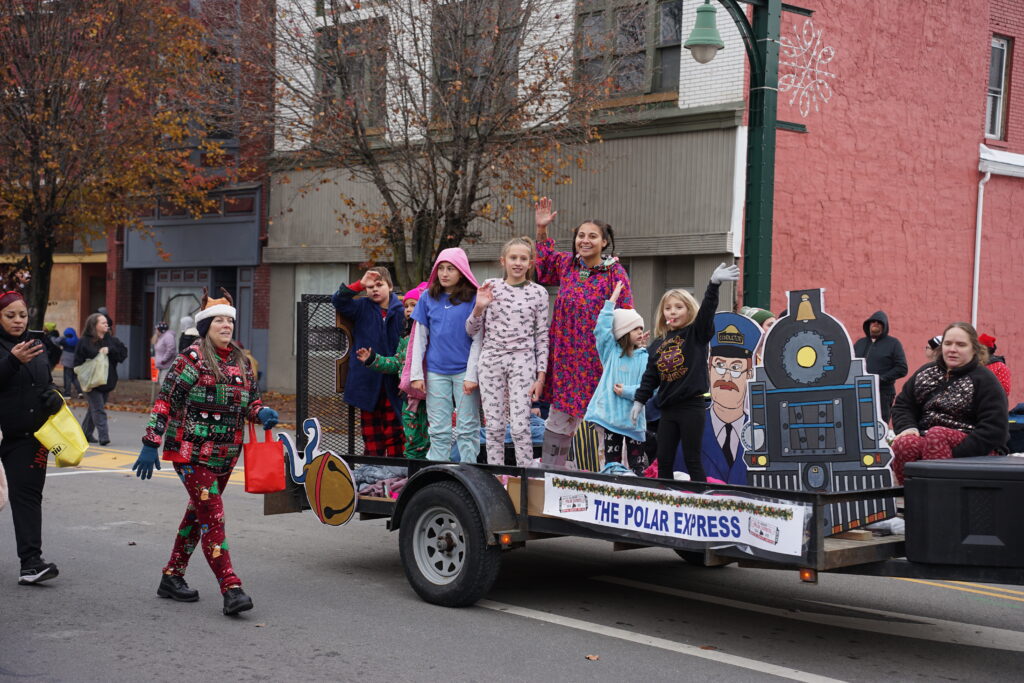 Photo of a truck trailer float in a christmas parade with children waving to the crowd