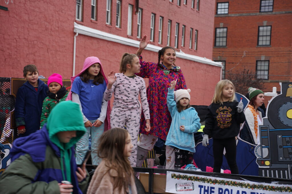 Photo of a truck trailer float in a christmas parade with children waving to the crowd