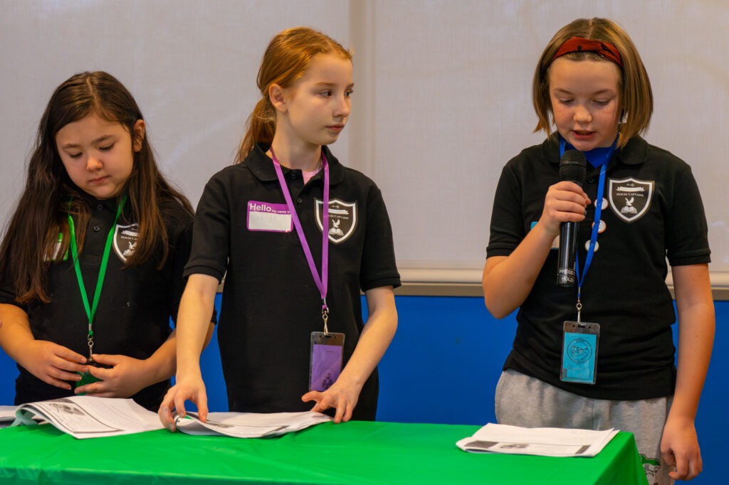 A student speaks into a microphone while reading from a sheet of paper. 