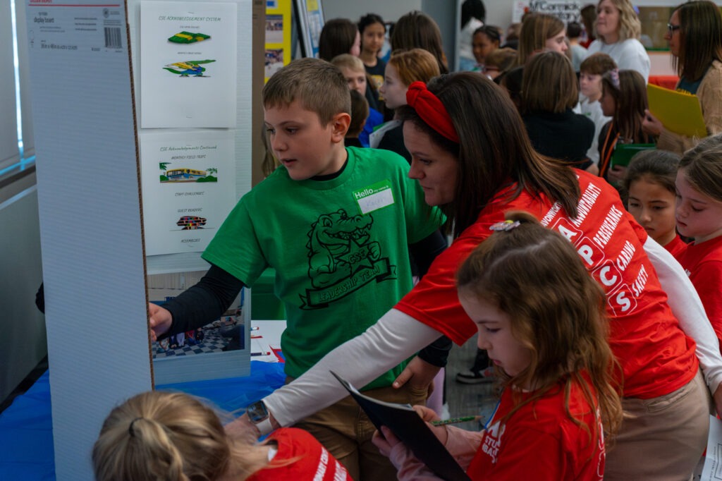 A student and a teacher point at a display poster on PBIS. 