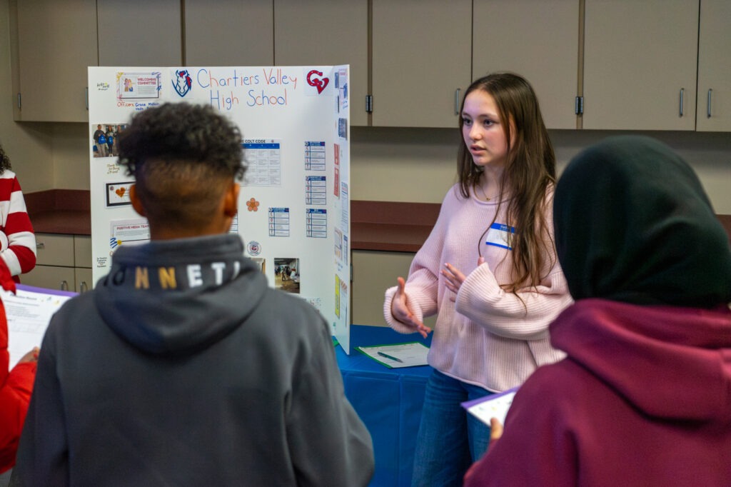 A student speaks with here peers in front of a PBIS poster.