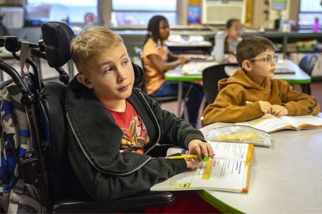 student in wheelchair sits at desk in classroom