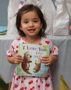 Child posing with new book titled "I Love You Like No Otter"